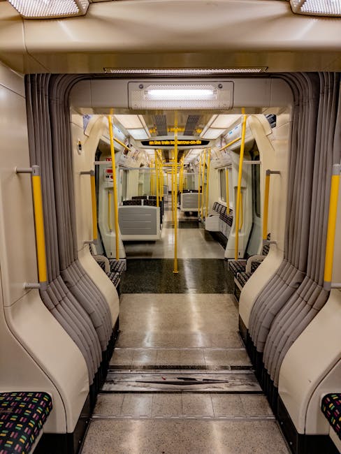 Inside a clean and well-maintained train carriage on the High Barnet tube service, showing a central aisle flanked by rows of fabric-upholstered seats with blue patterned covers and red armrests. The
